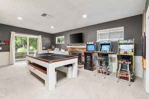 Una habitación con mesa de ping pong, juegos de arcade, televisor y chimenea.