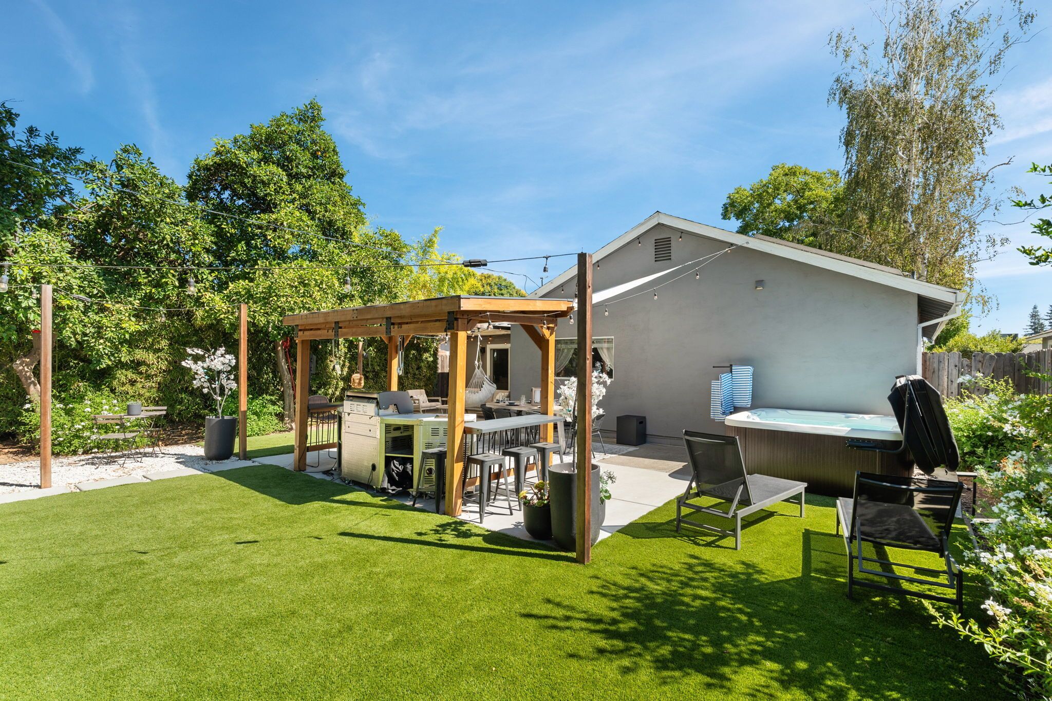 A backyard with a wooden pergola, outdoor seating, a grill, and a hot tub.