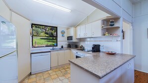 Una cocina compacta con armarios blancos, microondas integrado, cafetera y ventana con vistas a un jardín.