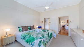 Un dormitorio con cama, mesita de noche, lámpara, ventilador de techo y una puerta que da a otra habitación.