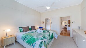 Ein Schlafzimmer mit einem Bett, Nachttisch, Lampe, Deckenventilator und einer Tür zu einem anderen Raum.