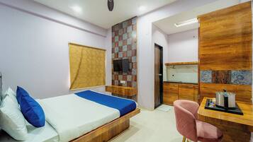 Habitación de hotel pequeña con cama, escritorio, silla y zona de ducha.