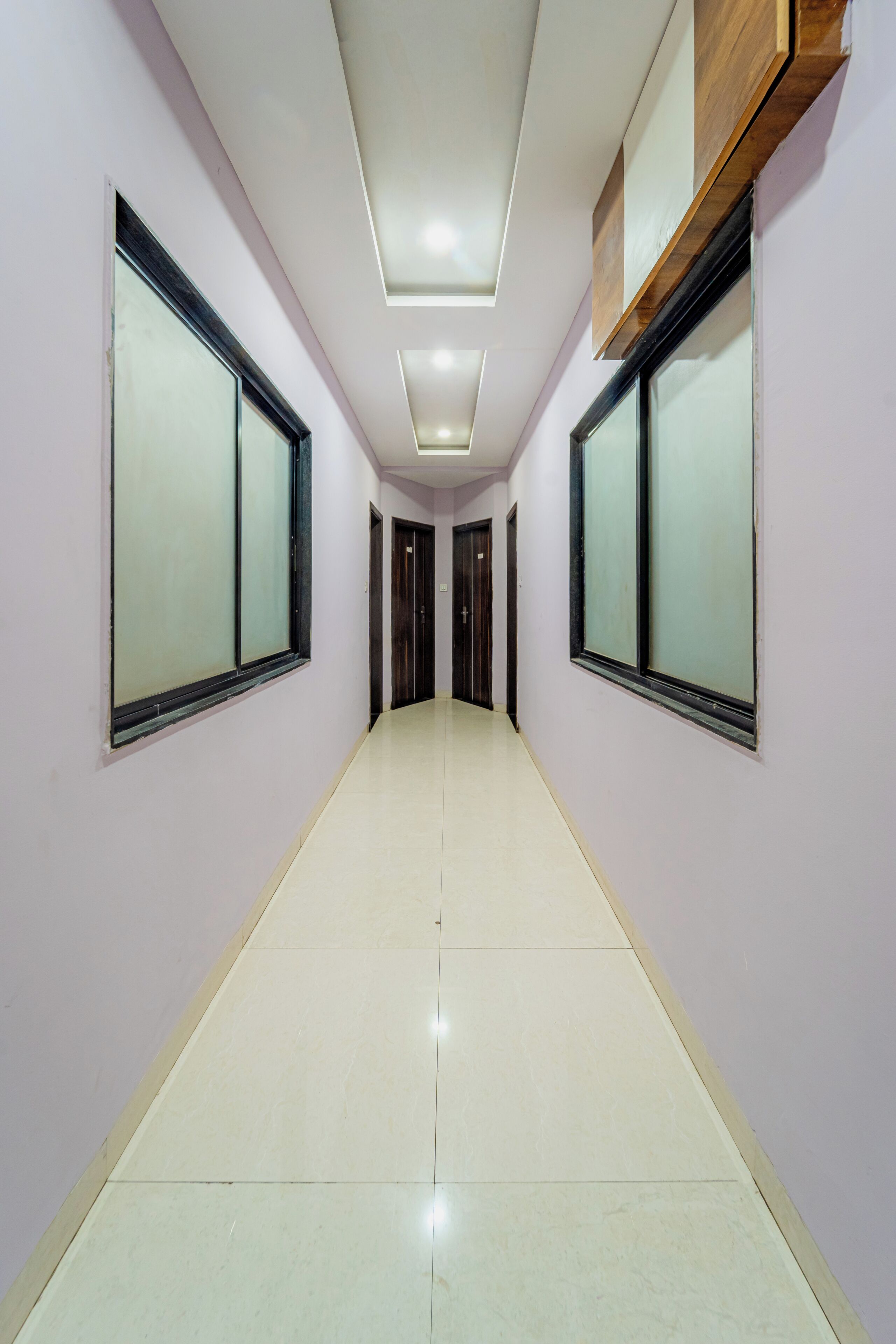 A hallway with a tiled floor, white walls, and large windows with black frames.