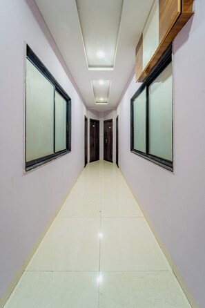A hallway with a tiled floor, white walls, and large windows with black frames. - Hotel Evanka by Navvarsh (Indore)