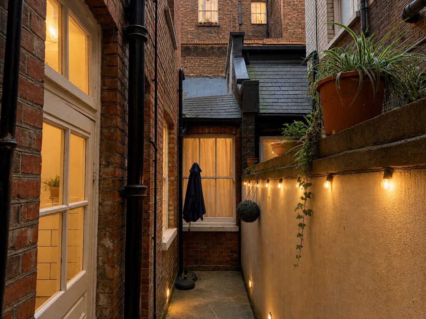 A narrow alleyway with brick walls, a window with curtains, a potted plant, and string lights.