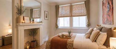 Un dormitorio con cama, mesita de noche, lámpara, ventana y chimenea.