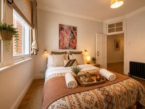 Une chambre bien éclairée, avec un lit, une table de chevet et une fenêtre agrémentée d’une plante.
