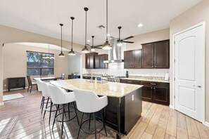 A modern kitchen with dark wood cabinets, a granite countertop, and a central island with bar stools. - Modern 5BR Pool Home Sleeps 15 Walk to Stadium (Glendale)