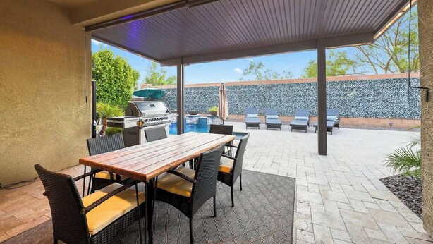 Un patio al aire libre con una parrilla, mesa de comedor y sillones.