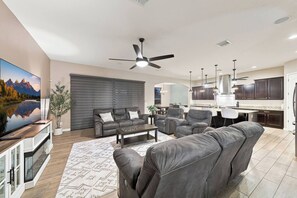 A modern living room with a large flat-screen TV, leather sofas, a coffee table, and a ceiling fan. - Modern 5BR Pool Home Sleeps 15 Walk to Stadium (Glendale)