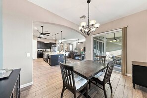 A spacious kitchen with dark cabinetry, a central island, and a dining area with a large wooden table and chairs. - Modern 5BR Pool Home Sleeps 15 Walk to Stadium (Glendale)