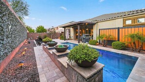 Un patio trasero con piscina, mobiliario exterior y zona de barbacoa.