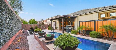 Un patio trasero con piscina, mobiliario exterior y zona de barbacoa.