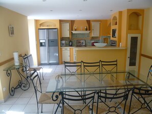 A dining area with a glass table and chairs, a refrigerator, and a microwave in the kitchen area. - Delphine's House (saint martin de l'arçon)