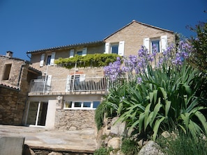 Ein Gebäude aus Stein mit einem Balkon, einer Steintreppe und purpurnen Blumen im Vordergrund.