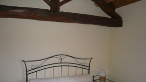 Uma cama de solteiro com estrutura de metal e colchão branco em quarto com vigas de madeira no teto.