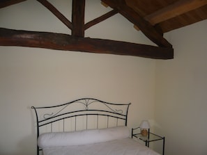 Ein Einzelbett mit Metallgestell und einer weißen Matratze in einem Zimmer mit Holzbalken an der Decke.