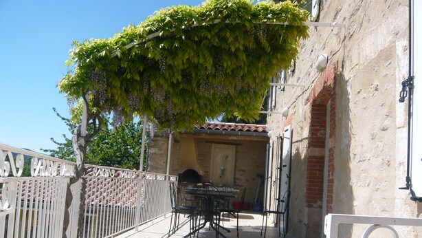 Um terraço com mesa e cadeiras, um muro branco e um edifício com parede de tijolos.