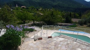 Uma piscina de pedra com grade de metal, rodeada por vegetação e ao fundo, montanhas.