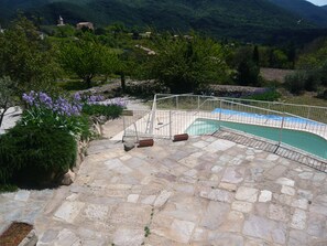 Ein steinerner Pool mit einem Metallzaun, umgeben von Grünpflanzen und einer Bergkulisse.
