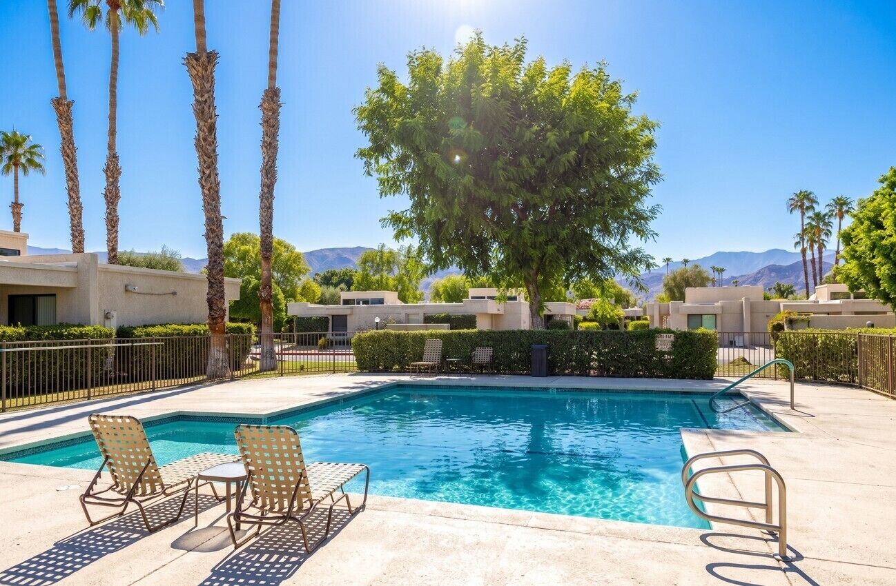 A swimming pool with lounge chairs, surrounded by palm trees and a clear sky.