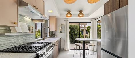 A modern kitchen with a stainless steel refrigerator, a gas stove, and a dining area with a table and chairs.