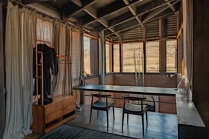 Una habitación con un escritorio de madera, dos sillas, un perchero y una ventana con vistas a un paisaje desértico.