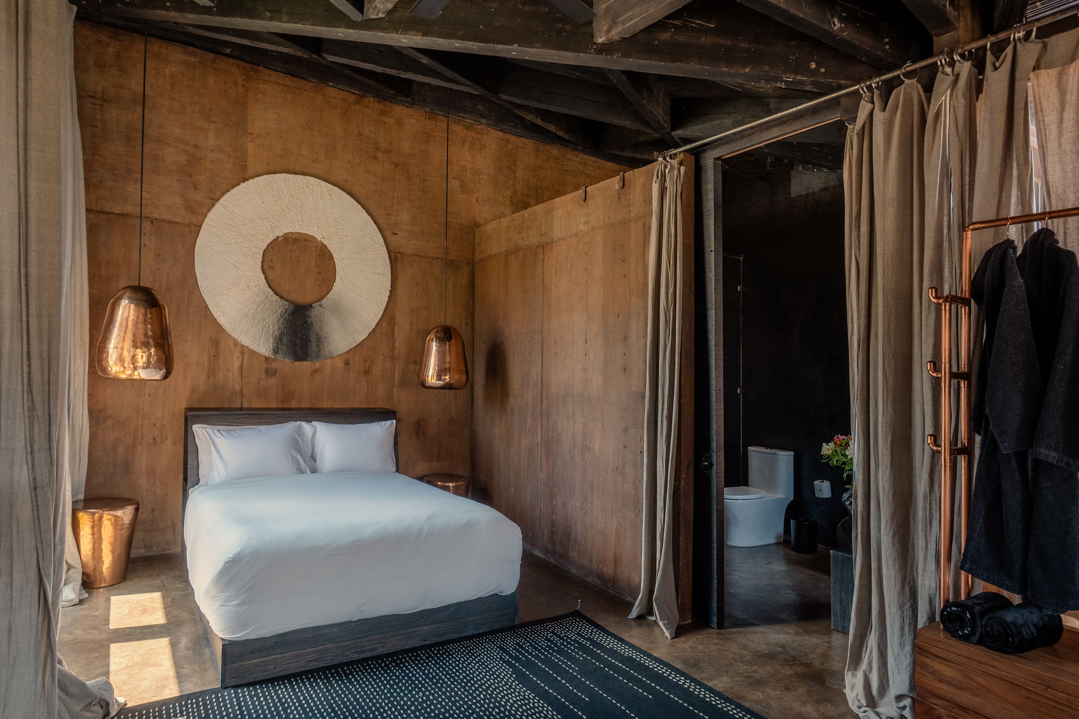 Un dormitorio con una cama grande, paredes de madera, un adorno circular en la pared y un baño visible a través de una puerta abierta.