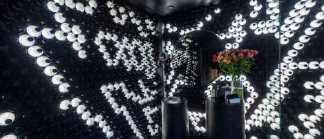 A room with a patterned wall, a mirror, and a vase with flowers.