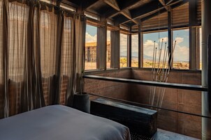 Una habitación con una cama, un ventanal con vistas al paisaje y una pequeña mesa con una planta.