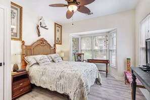 A bedroom with a bed, a nightstand, a desk, a chair, a window, and a ceiling fan. - 3BR Ocean Breeze Escape | Walk to Beach at Coligny (Hilton Head Island)