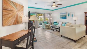 A living room with a dining area, a ceiling fan, and a view through large windows. - 3BR Ocean Breeze Escape | Walk to Beach at Coligny (Hilton Head Island)