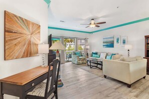 A living room with a dining area, a ceiling fan, and a view through large windows. - 3BR Ocean Breeze Escape | Walk to Beach at Coligny (Hilton Head Island)
