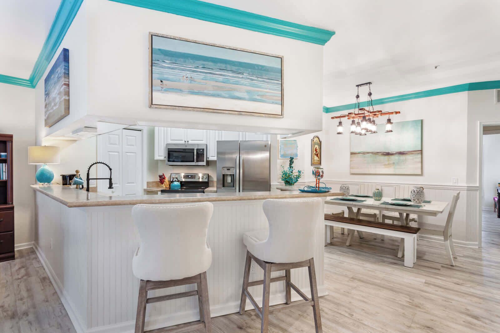 A modern kitchen with white cabinetry, a central island with bar stools, and a dining area with a white table and chairs.
