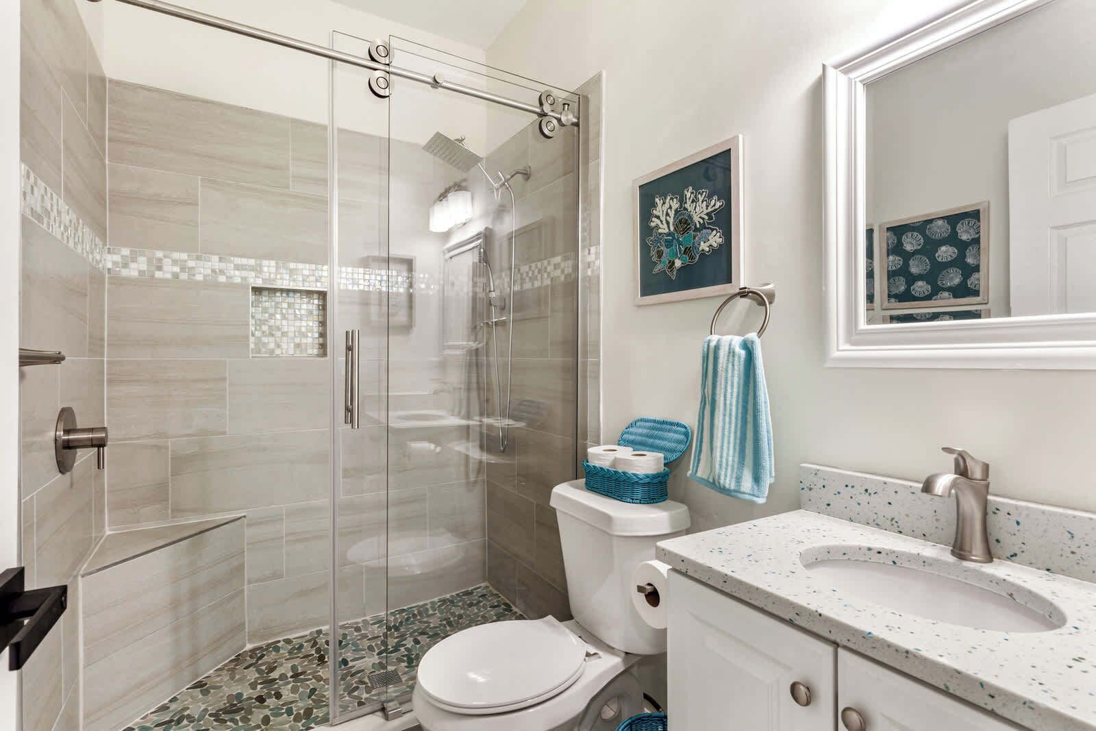 Une salle de bain moderne dotée d’une douche à parois de verre, de toilettes, d’un lavabo avec un plan de travail à motifs et d’un miroir encadré.
