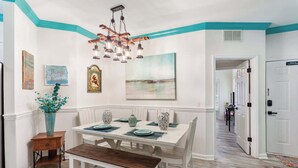 A dining area with a white table set for four, a wooden bench, and a hanging light fixture. - 3BR Ocean Breeze Escape | Walk to Beach at Coligny (Hilton Head Island)