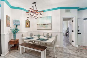 A dining area with a white table set for four, a wooden bench, and a hanging light fixture. - 3BR Ocean Breeze Escape | Walk to Beach at Coligny (Hilton Head Island)