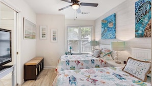 A bedroom with two beds, a ceiling fan, a TV, and artwork on the walls. - 3BR Ocean Breeze Escape | Walk to Beach at Coligny (Hilton Head Island)