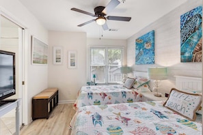 A bedroom with two beds, a ceiling fan, a TV, and artwork on the walls. - 3BR Ocean Breeze Escape | Walk to Beach at Coligny (Hilton Head Island)