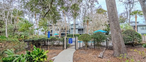 A pathway leading to a gated area with a pool, surrounded by trees and greenery.