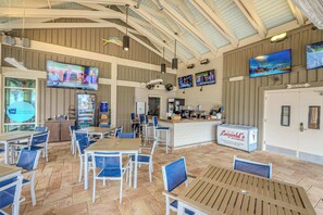 A spacious indoor area with multiple tables and chairs, a counter with a beverage station, and several flat-screen TVs mounted on the walls. - 3BR Ocean Breeze Escape | Walk to Beach at Coligny (Hilton Head Island)
