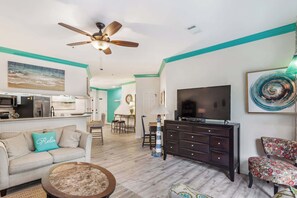 A living room with a sofa, coffee table, TV, and a ceiling fan. - 3BR Ocean Breeze Escape | Walk to Beach at Coligny (Hilton Head Island)