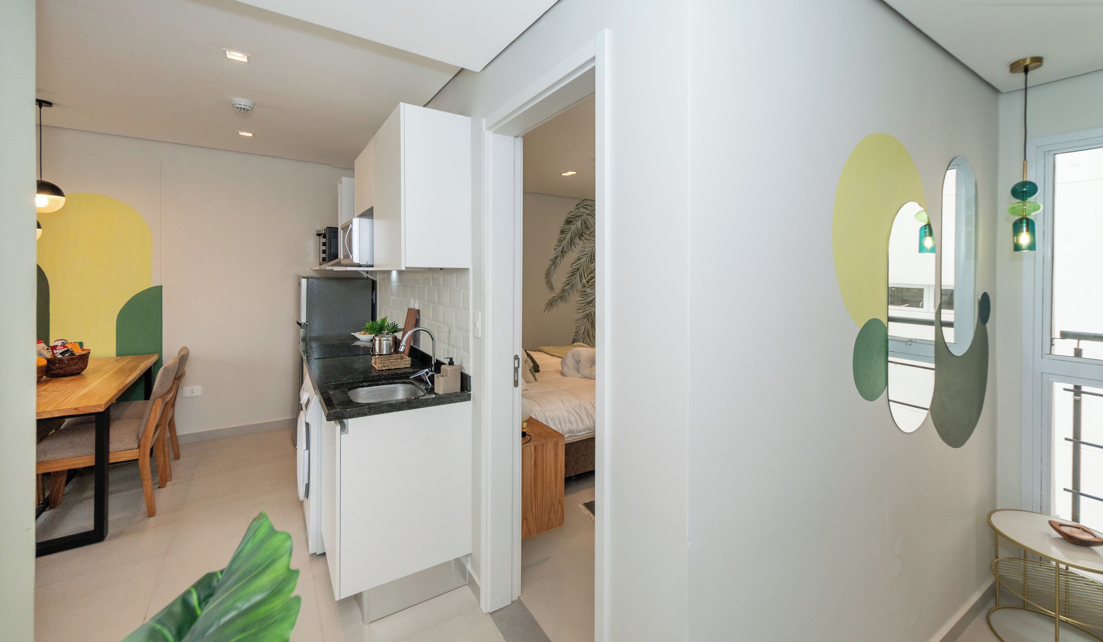 Una cocina moderna con armarios blancos, encimera negra y zona de comedor con mesa y sillas de madera.