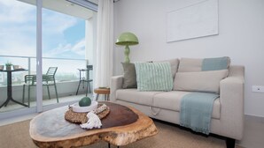 Ein modernes Wohnzimmer mit einer Couch, einem Couchtisch und Blick auf die Stadt durch große Fenster.
