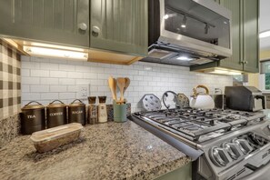 Uma cozinha com bancadas de granito, eletrodomésticos de aço inoxidável e utensílios de madeira.