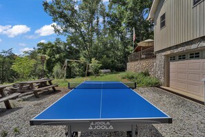 Uma mesa de ping pong ao ar livre com um muro de pedra e um deck de madeira ao fundo.