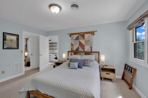 A bedroom with a bed, bedside lamps, a quilted headboard, a window with curtains, and a door leading to another room. - Private Blue Ridge 3BR Haven, Luxury Hot Tub (Bakersville)