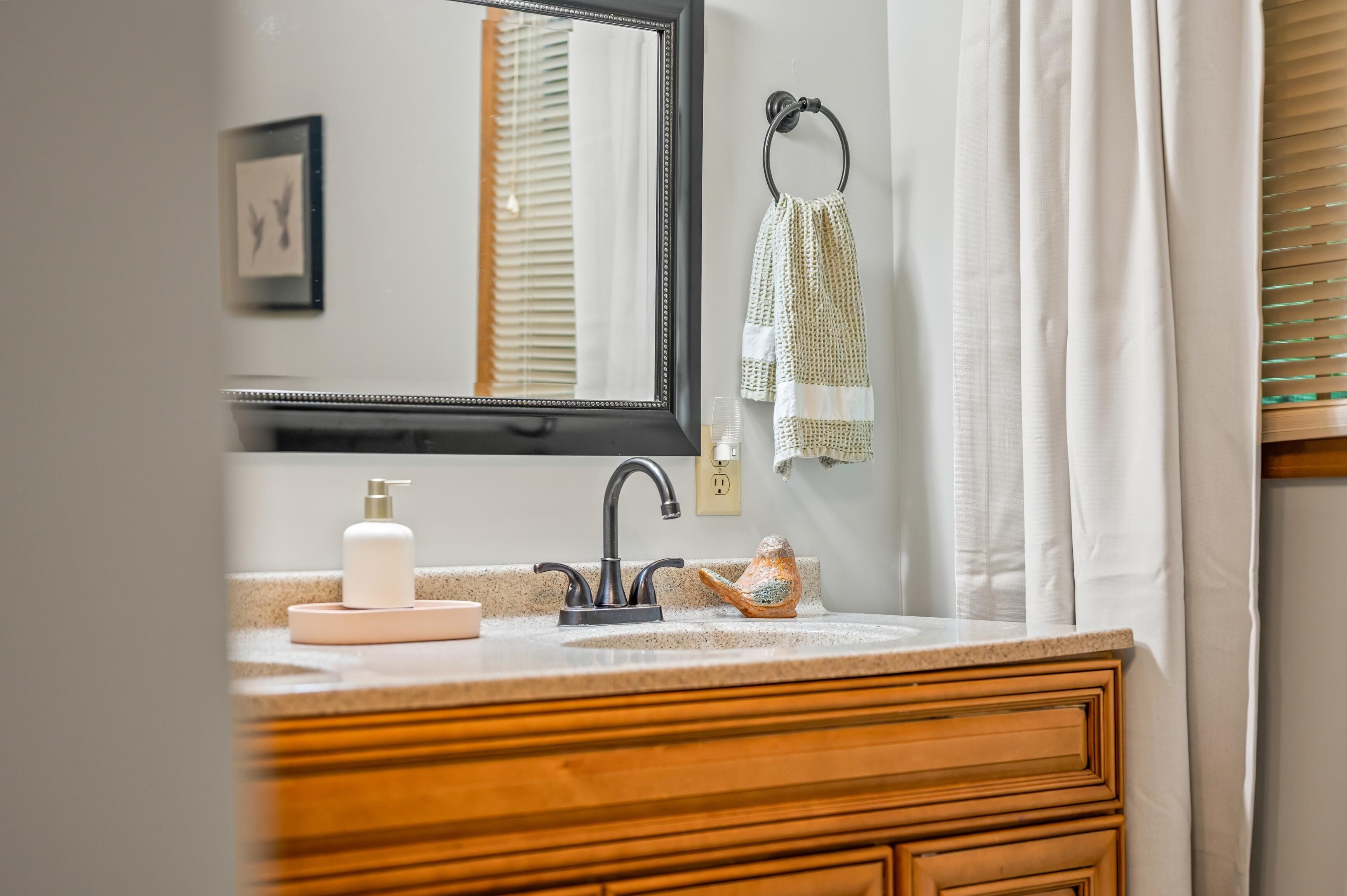 Une salle de bain équipée d’un lavabo, d’un miroir, d’un porte-serviettes et d’une fenêtre avec des stores.