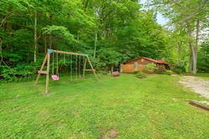 A wooden swing set in a grassy yard with a small cabin in the background.