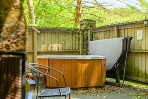 Eine Holzterrasse mit Whirlpool, überdachtem Tisch und einem Stuhl.
